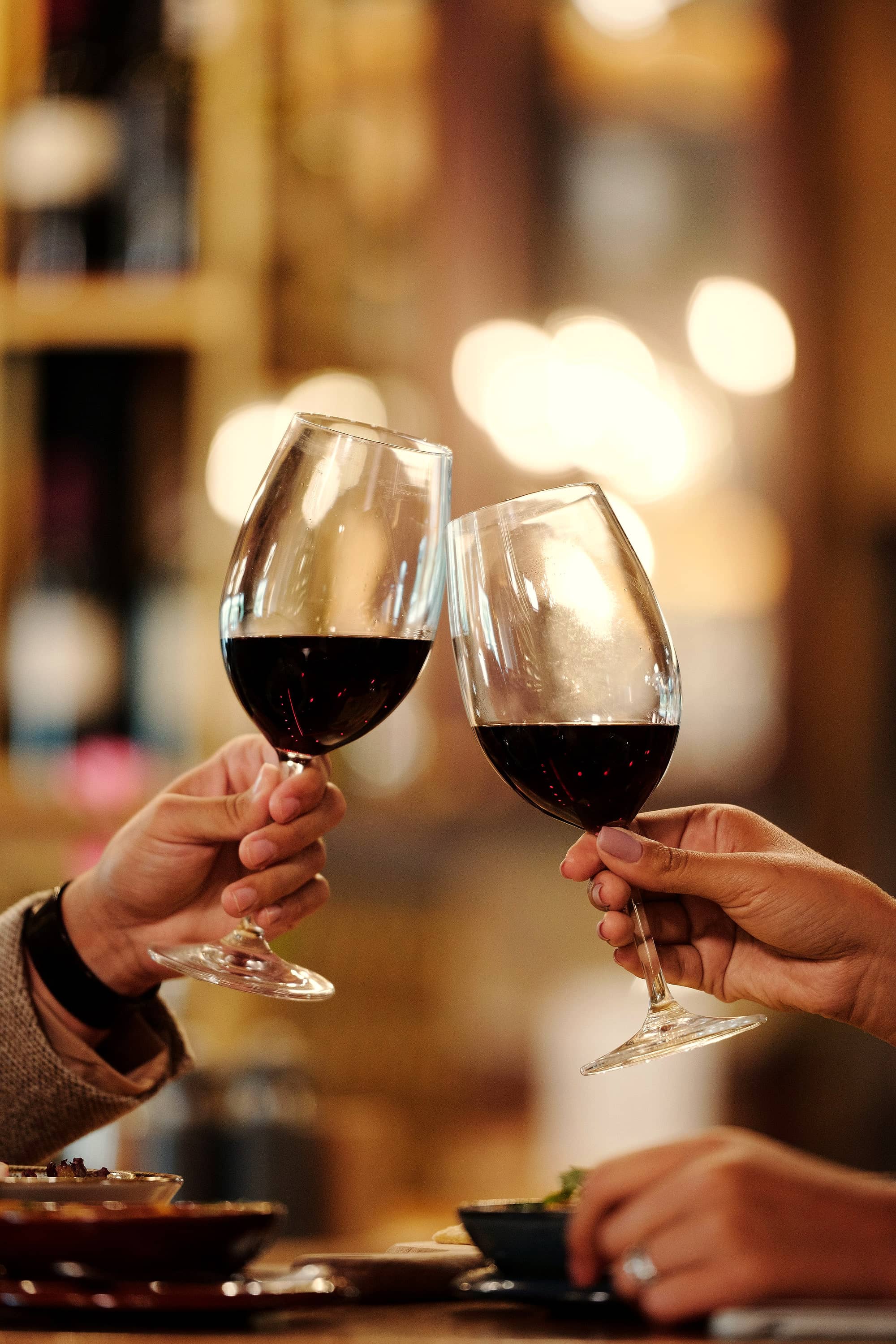 Zwei Gläser Rotwein stoßen im warmen Licht an